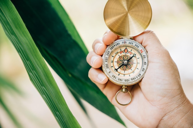 Un gros plan d'une main tenant une boussole au cœur d'une forêt verte Cette image laisse de la place au texte et signifie le style de vie de voyage et la gestion stratégique d'une entreprise prospère