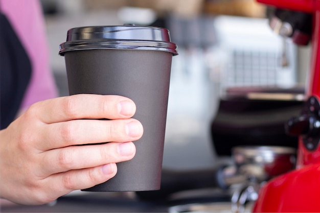 Gros plan sur la main tenant le café chaud dans une tasse en papier