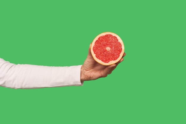 Gros plan d'une main tenant des fruits savoureux de pamplemousse juteux tranchés pour la nourriture végétarienne biologique naturelle de désintoxication pleine de vitamines alimentation saine et concept de perte de poids intérieur isolé sur fond vert