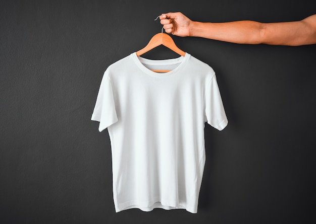 Gros plan de la main tenant un t-shirt blanc suspendu à un cintre en bois