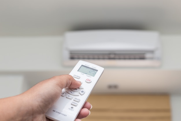 Gros plan main tenant la télécommande dirigée sur le climatiseur