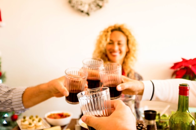 Photo gros plan sur une main tenant un verre de vin tintant avec trois autres personnes à la maison ou au restaurant en train de manger et de boire ensemble - femme bouclée et belle à l'arrière-plan