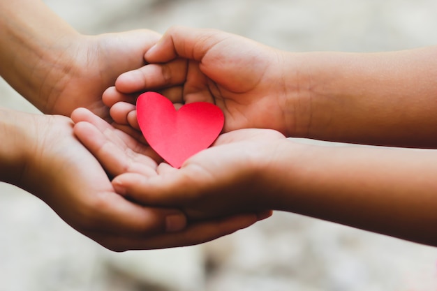 Photo gros plan des mains adulte et enfant, tenant un coeur rouge.