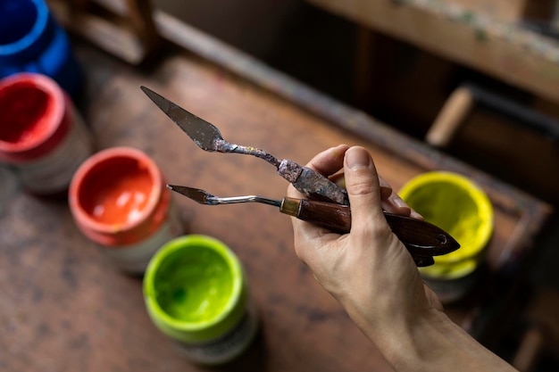 Gros plan des mains d'une artiste latino-américaine méconnaissable montrant les couteaux à palette qu'elle utilise pour peindre dans son studio d'art Concept d'artiste et de passe-temps