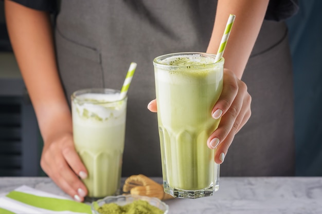 Gros plan, des mains de barista tendent un verre. Boisson au thé vert matcha dans un verre avec une paille. Latte utile