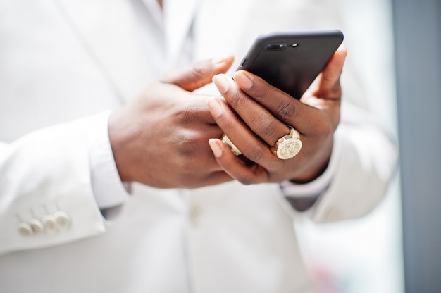 Gros plan des mains de beau gentleman afro-américain en tenue de soirée à la recherche de téléphone mobile.