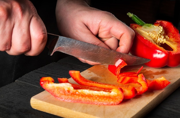 Gros plan sur les mains d'un chef coupant des poivrons sur une planche à découper