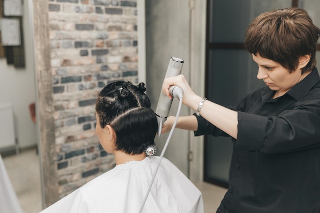 Gros plan des mains d'un coiffeur séchant les cheveux des femmes avec un sèche-cheveux coupe courte et coiffage