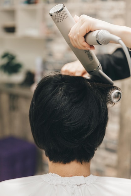 Gros plan des mains d'un coiffeur séchant les cheveux des femmes avec un sèche-cheveux coupe courte et coiffage