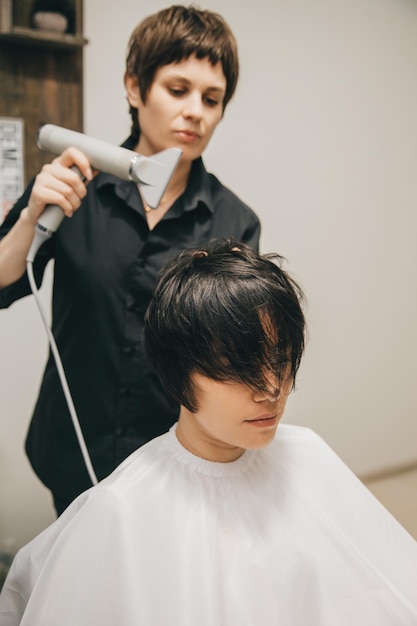 Gros plan des mains d'un coiffeur séchant les cheveux des femmes avec un sèche-cheveux coupe courte et coiffage