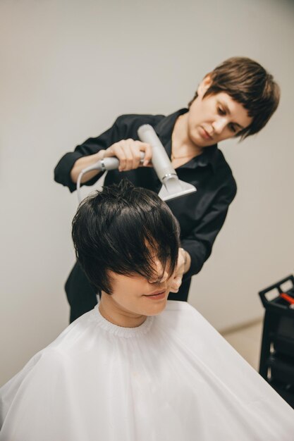 Gros plan des mains d'un coiffeur séchant les cheveux des femmes avec un sèche-cheveux coupe courte et coiffage