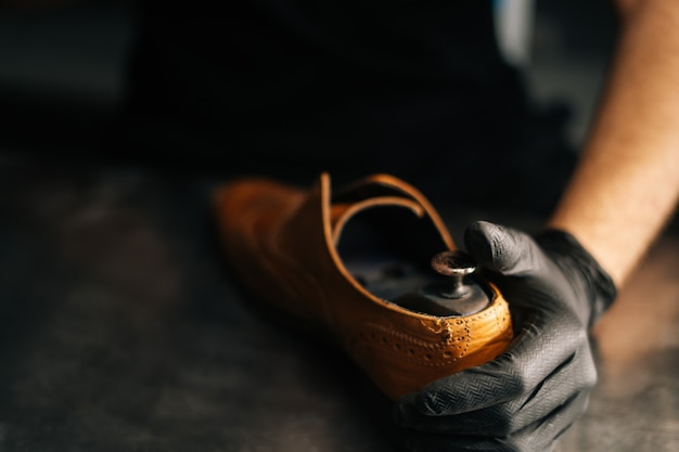 Gros plan des mains d'un cordonnier portant des gants noirs insère un bloc de chaussures en bois dans la lumière usée ...