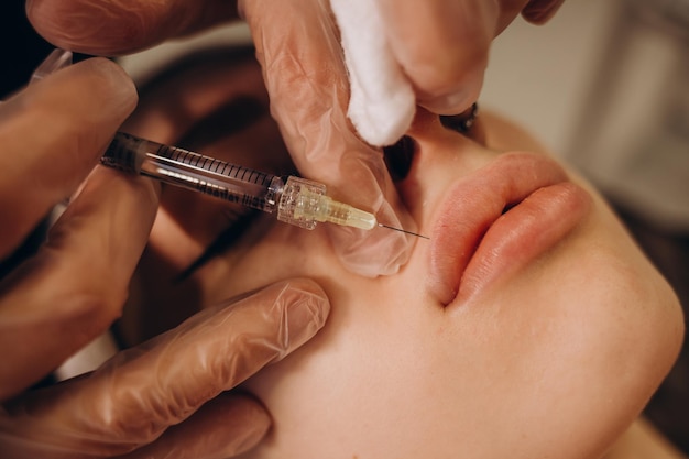 Gros plan des mains d'un cosmétologue faisant une injection de botox dans les lèvres féminines Elle tient une seringue La belle jeune femme reçoit la procédure avec plaisir