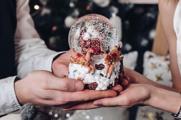 Gros plan des mains d'un couple masculin et féminin tenant une statuette du Père Noël avec des cerfs entourés de flocons de neige. Heureuse famille appréciant le conte de fées Joyeux Noël et bonne année