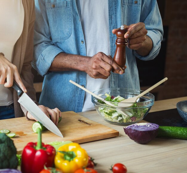 Gros plan des mains de couples noirs préparant une salade de légumes sains ensemble dans la cuisine