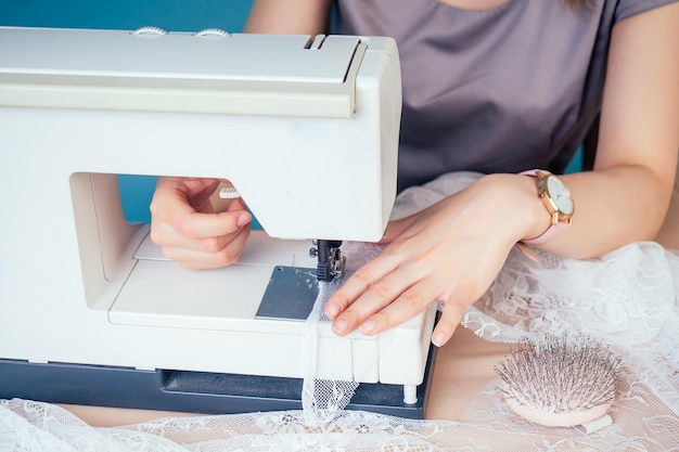 Gros plan des mains de couturière tailleur couturière enfiler l'aiguille sur la machine à coudre sur un fond bleu dans le studio Le concept de création d'une nouvelle collection de vêtements