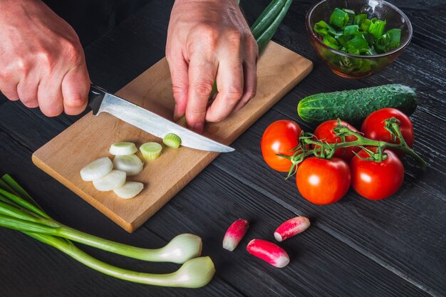 Le gros plan des mains du chef coupe les jeunes oignons verts. Salade de cuisson dans la cuisine du restaurant. Ensemble de légumes pour un régime de salade.