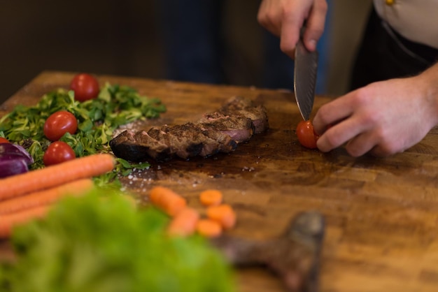 gros plan des mains du chef dans la cuisine de l'hôtel ou du restaurant préparant un steak de boeuf avec une décoration végétale