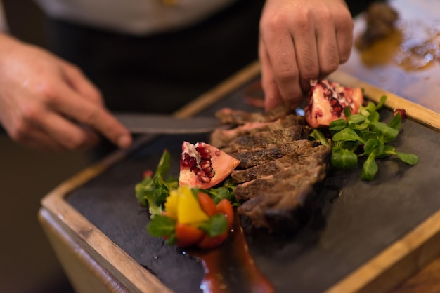 gros plan des mains du chef dans la cuisine de l'hôtel ou du restaurant préparant un steak de boeuf avec une décoration végétale