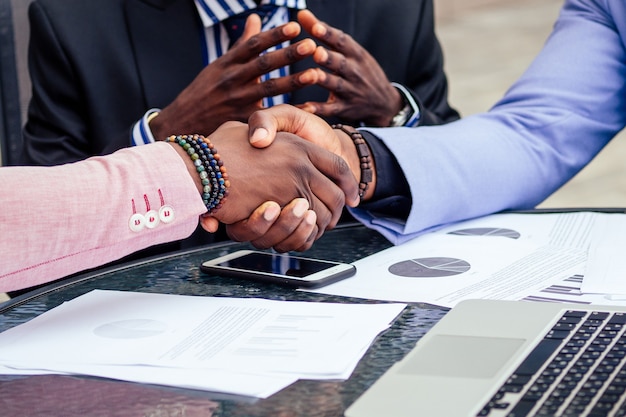 Gros plan sur les mains du groupe trois élégants amis d'affaires afro-américains se serrant la main dans un café d'été à l'extérieur. concept de bonne affaire réussie.