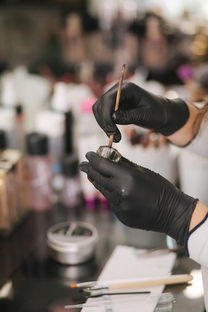 Gros plan des mains du maître des sourcils dans des gants noirs à l'aide d'un pinceau et de henné
