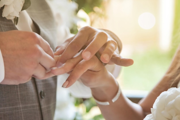 Gros plan des mains du marié tenant la main de la mariée et mettant l'anneau de mariage sur la fiancée au doigt