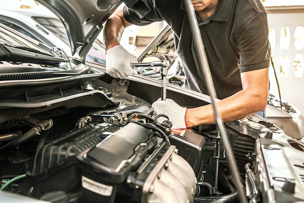 Photo gros plan sur les mains du mécanicien automobile utilisant la clé pour entretenir le moteur de la voiture.