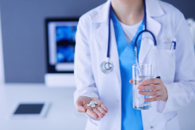 Gros plan sur les mains du médecin tenant des pilules et un verre d'eau.