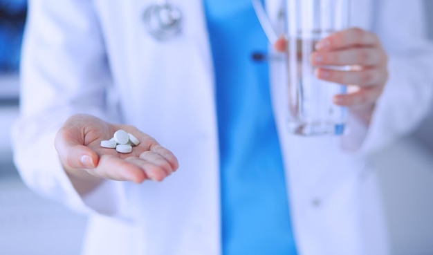 Gros plan des mains du médecin tenant des pilules et un verre d'eau