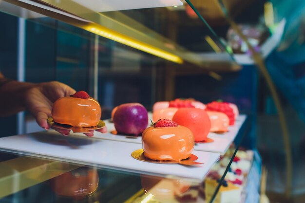 Gros plan des mains du vendeur sortant le gâteau de la vitrine de la boulangerie