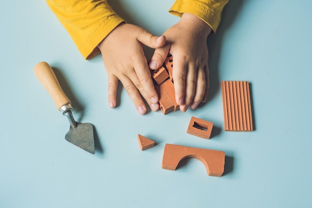 Gros plan sur les mains de l'enfant jouant avec de vraies petites briques d'argile à la table. Tout-petit s'amusant et construisant de vraies petites briques d'argile. Apprentissage précoce. Développement de jouets. Concept de construction