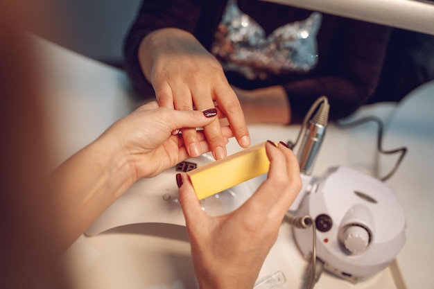 Gros plan sur les mains d'une esthéticienne polissant les ongles des clientes avec une lime à ongles au salon de beauté.