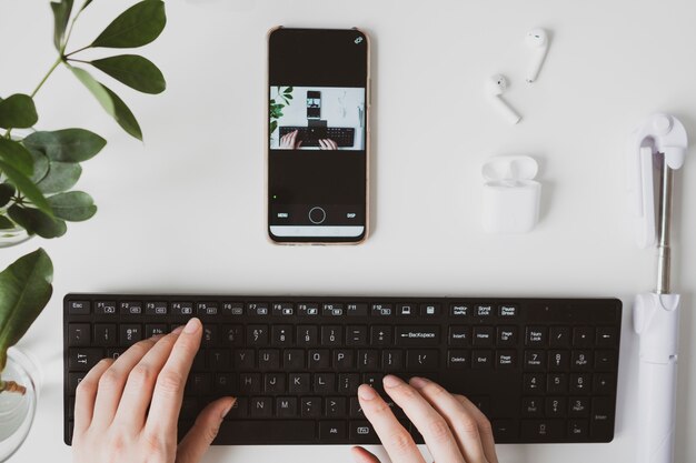 Gros plan des mains féminines avec claviers et smartphone sur le lieu de travail blanc