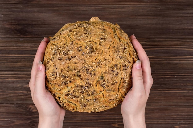 Gros plan de mains féminines sur une table sombre en bois avec vue de dessus de pain frais Pain sans levure fait maison avec des graines de chia graines de lin graines de tournesol graines de sésame