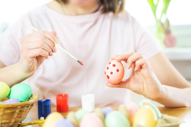 Gros plan sur des mains féminines tenant un oeuf de Pâques et peignant avec un pinceau Préparation à Pâques