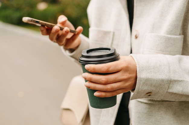 Gros plan de mains féminines tenant un téléphone et une tasse de café chaud pour aller