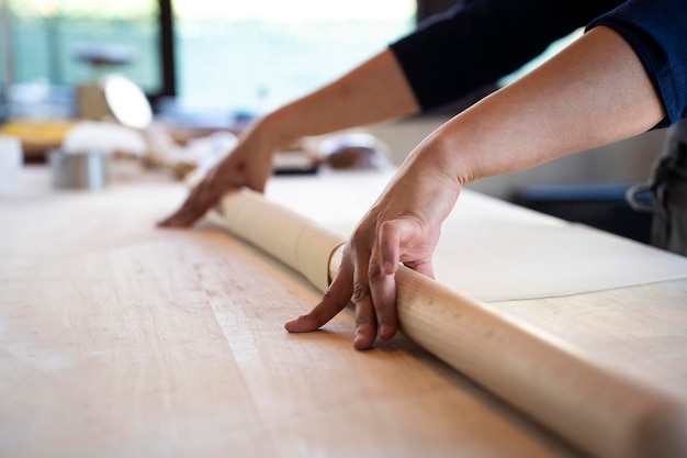 Gros plan des mains féminines travaillant avec un rouleau à pâtisserie pour les pâtes fraîches italiennes Mains féminines roulant pour la pâte fraîche sur la table en bois concept de cuisine et de pâtes fraîches faites maison