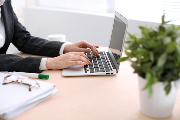 Gros plan sur des mains de femme d'affaires tapant sur un ordinateur portable dans le bureau de couleur blanche.