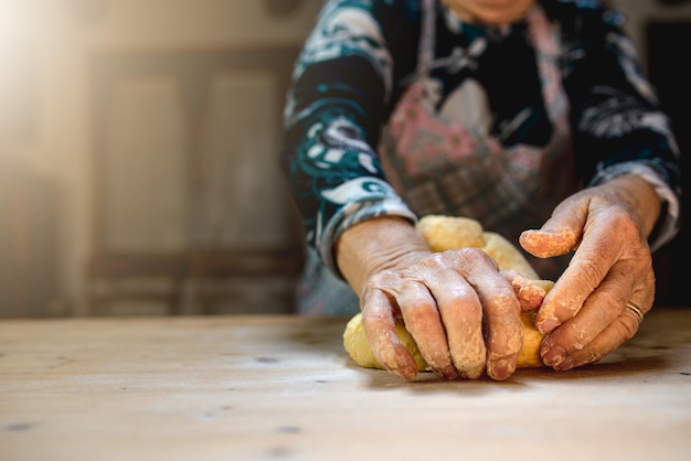 Gros plan des mains d'une femme âgée pétrissant la pâte dans la cuisine