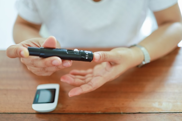 Gros plan des mains de femme à l'aide d'une lancette sur le doigt pour vérifier le taux de sucre dans le sang par glucomètre. Utiliser comme concept de médecine, de diabète, de glycémie, de soins de santé et de personnes.