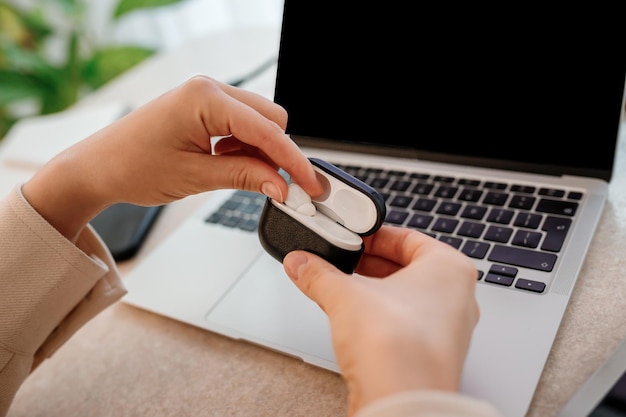 Gros plan sur des mains de femme assises dans un bureau à domicile avec un ordinateur portable met des écouteurs sans fil dans un étui