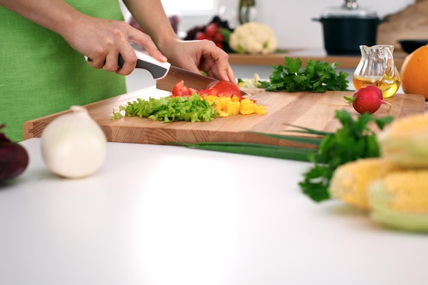 Gros plan sur les mains d'une femme cuisinant dans la cuisine. Femme au foyer coupant une salade fraîche. Concept de cuisine végétarienne et saine.