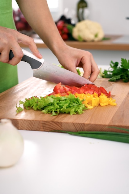 Gros plan sur les mains d'une femme cuisinant dans la cuisine. Femme au foyer coupant une salade fraîche. Concept de cuisine végétarienne et saine.