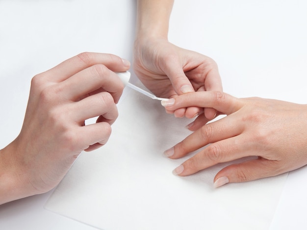 Gros plan des mains de la femme dans un salon de manucure recevant une manucure sur fond blanc