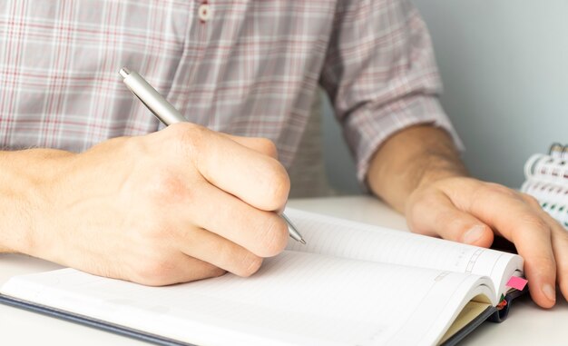 Gros plan des mains de la femme écrivant dans un bloc-notes en spirale placé sur un bureau en bois avec divers articles