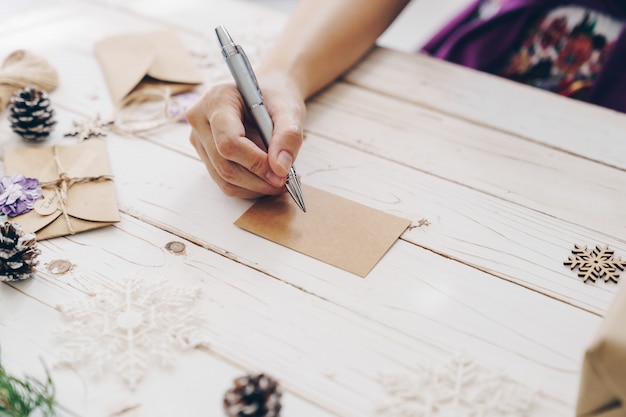 Gros plan des mains femme écrivant liste de souhaits vide et carte de Noël sur table en bois avec décoration de Noël.