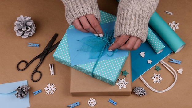 Gros plan des mains de femme emballant et emballant des coffrets cadeaux de Noël avec du papier bleu, ajoutant des feuilles d'enveloppe et de squelette, vue grand angle