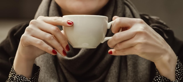 Gros plan des mains de femme avec manucure rouge tenant une tasse de café aux tons vintage