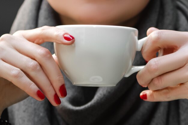 Gros plan des mains de femme avec manucure rouge tenant une tasse de café