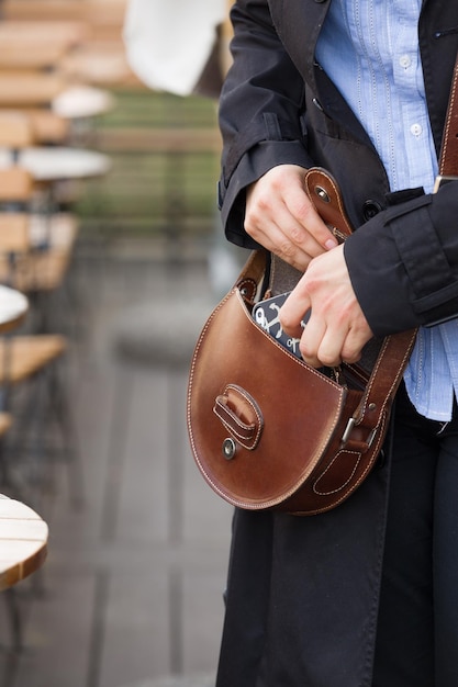 Gros plan sur les mains d'une femme mettant un smartphone dans un sac à main en cuir marron